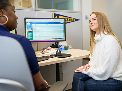 Staff member helps student while sitting at desk